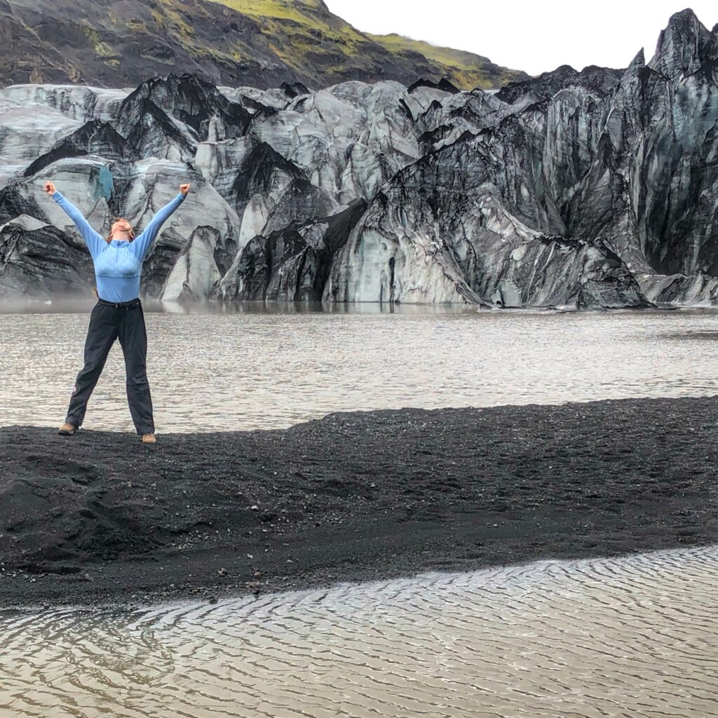 Girl in victory position, standing in front of a glacier. Illustrating the power of place.